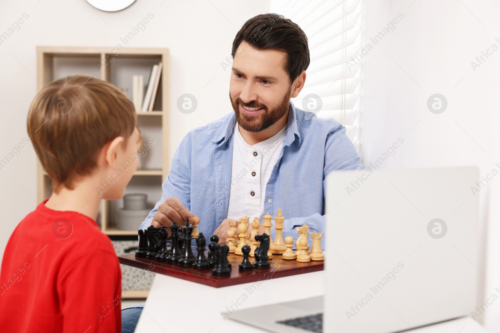 Photo of Father and son playing chess following online lesson in room