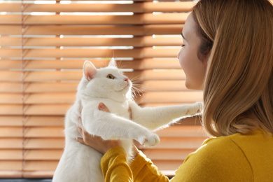 Photo of Young woman with her beautiful white cat near window at home. Fluffy pet