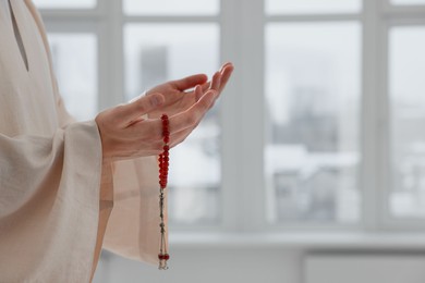 Photo of Muslim man with misbaha praying near window indoors, closeup. Space for text