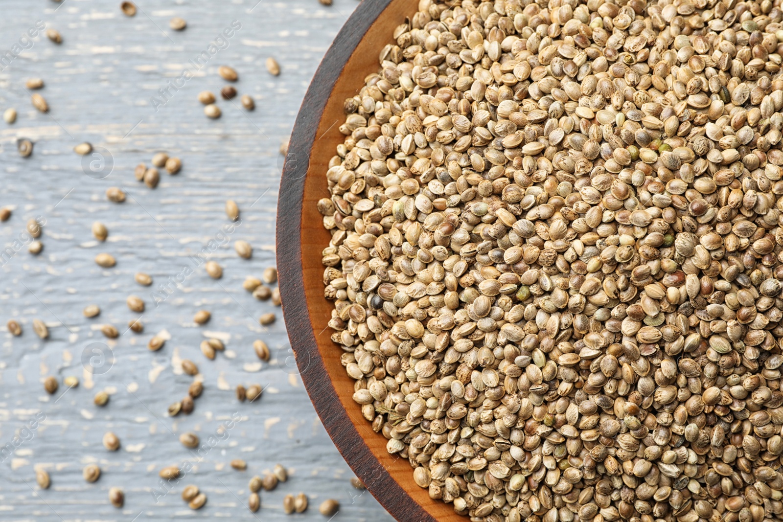Photo of Organic hemp seeds in bowl on grey wooden table, top view