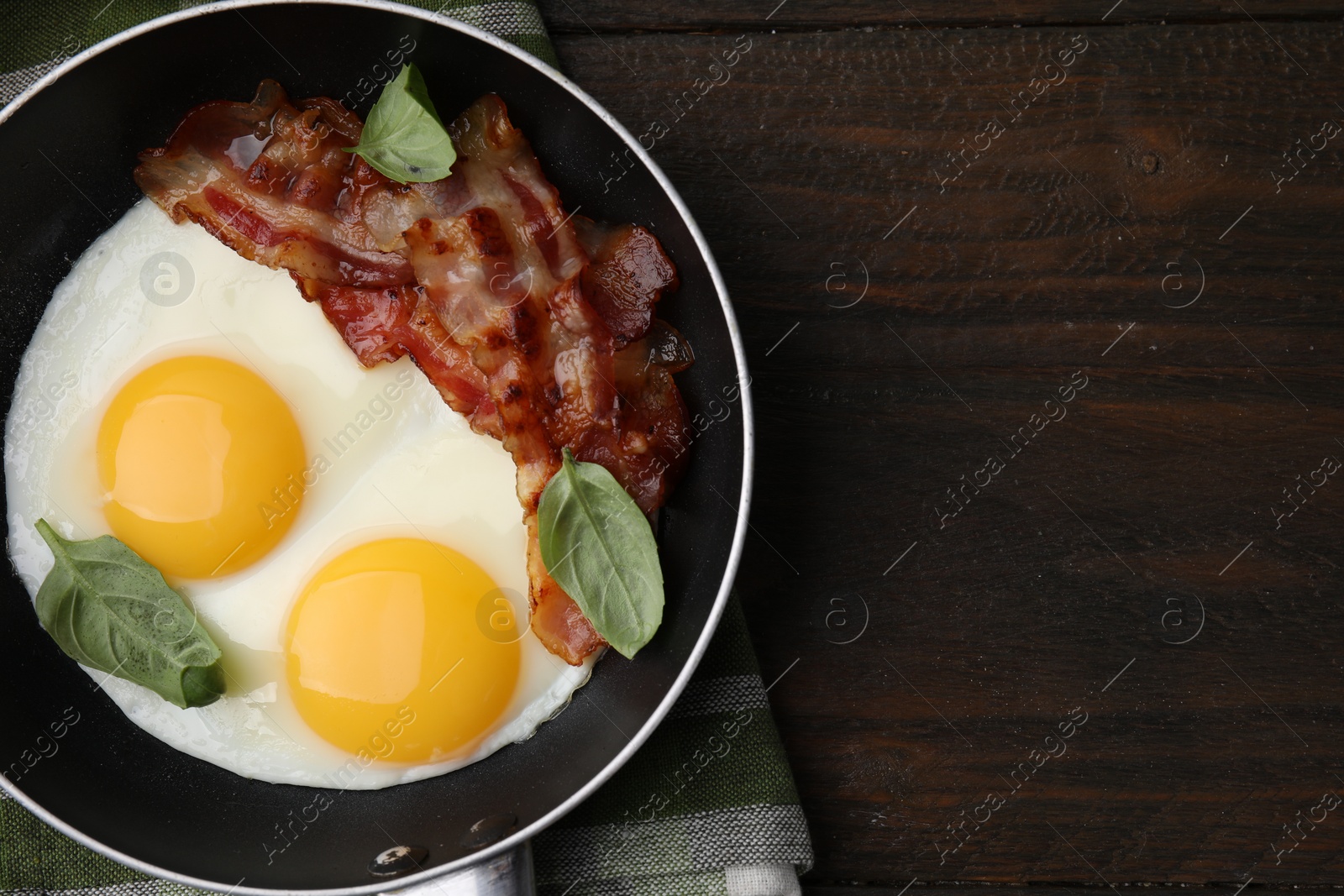 Photo of Fried eggs, bacon and basil in frying pan on wooden table, top view. Space for text