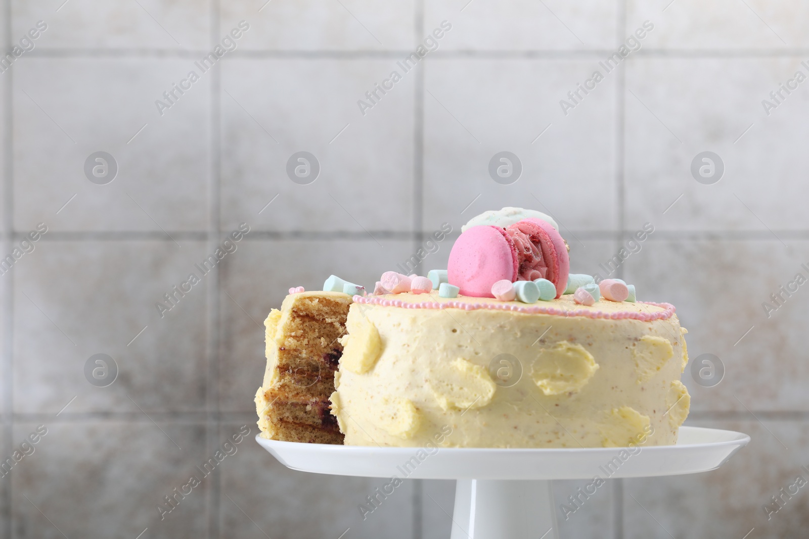 Photo of Delicious cake decorated with macarons and marshmallows against light tiled background