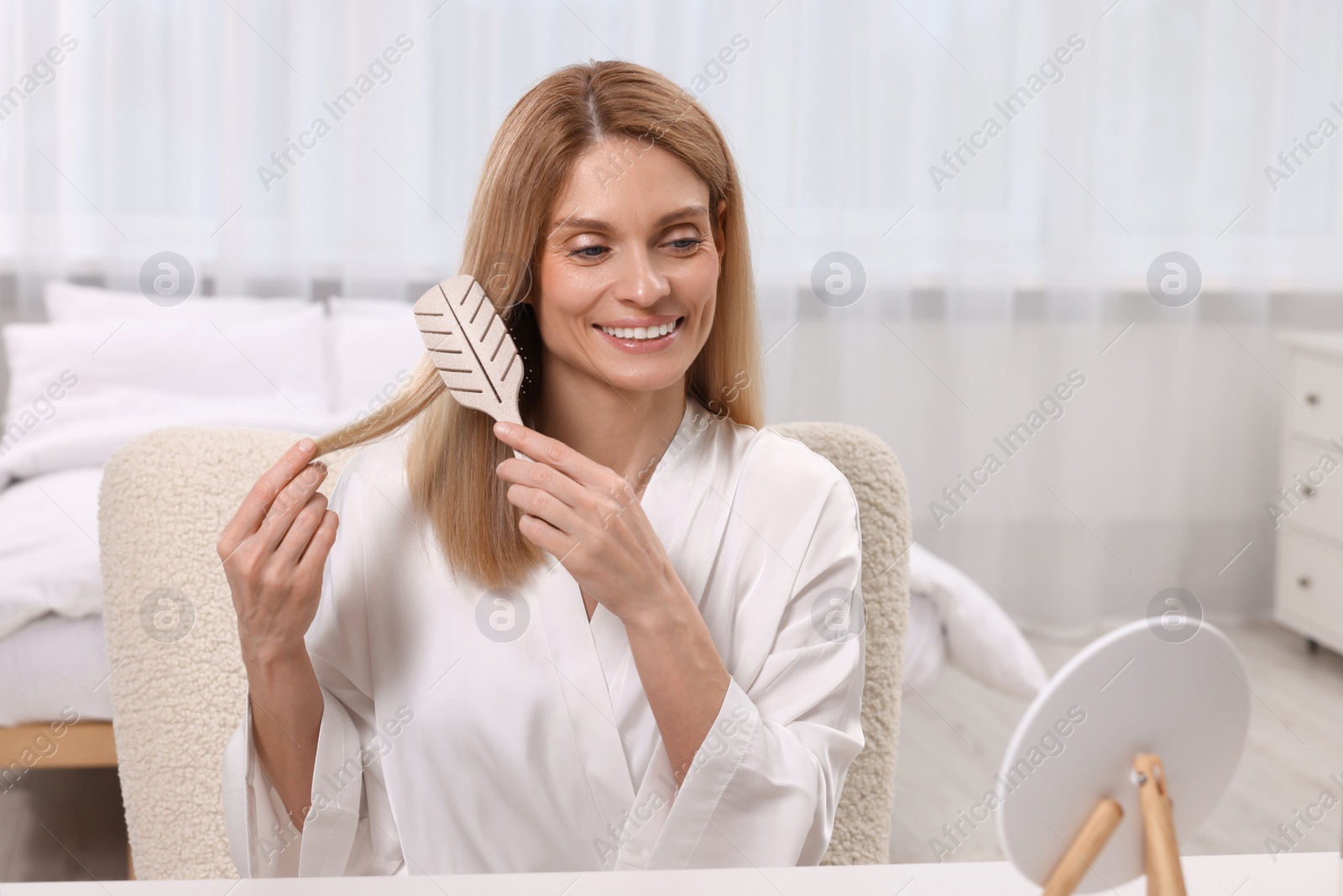 Photo of Beautiful woman brushing her hair at vanity in bedroom