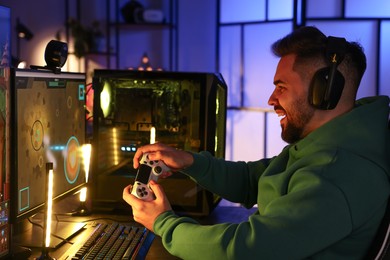 Photo of Man playing video games with controller at table indoors