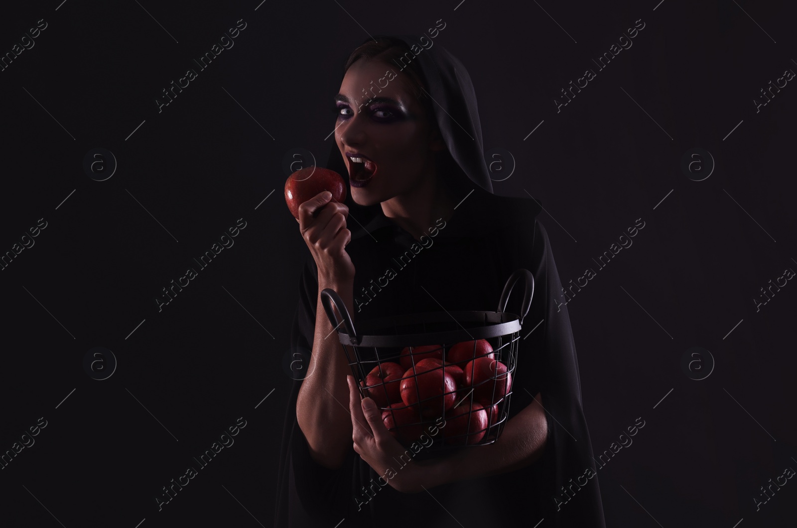 Photo of Mysterious witch eating apple on black background