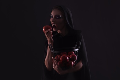 Photo of Mysterious witch eating apple on black background