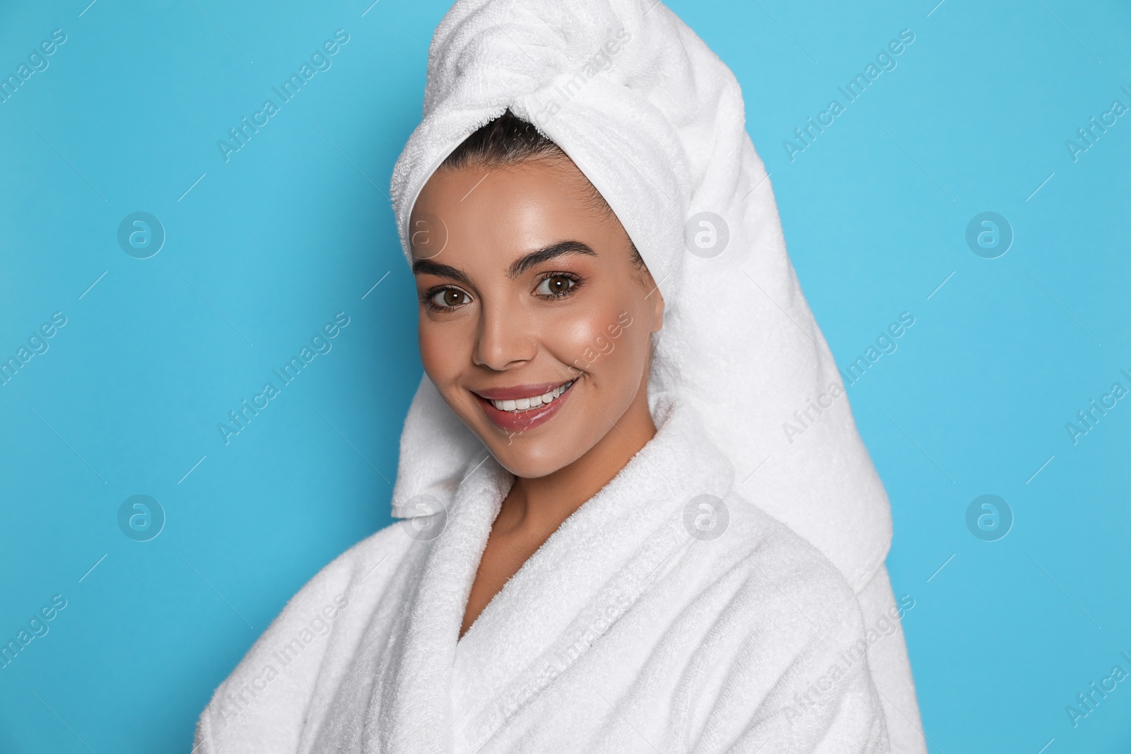 Photo of Beautiful young woman wearing bathrobe and towel on head against light blue background