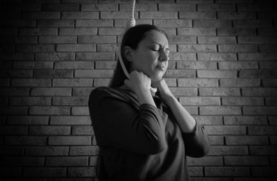 Image of Depressed woman with rope noose on neck near brick wall. Suicide concept