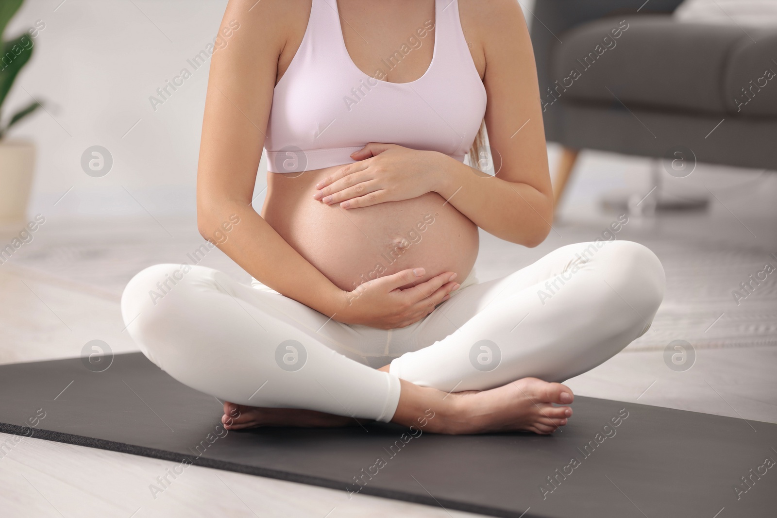 Photo of Pregnant woman sitting on yoga mat at home, closeup