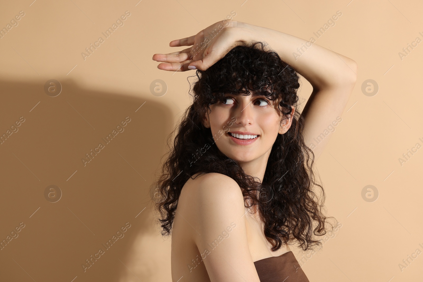 Photo of Portrait of beautiful young woman in sunlight on beige background, space for text