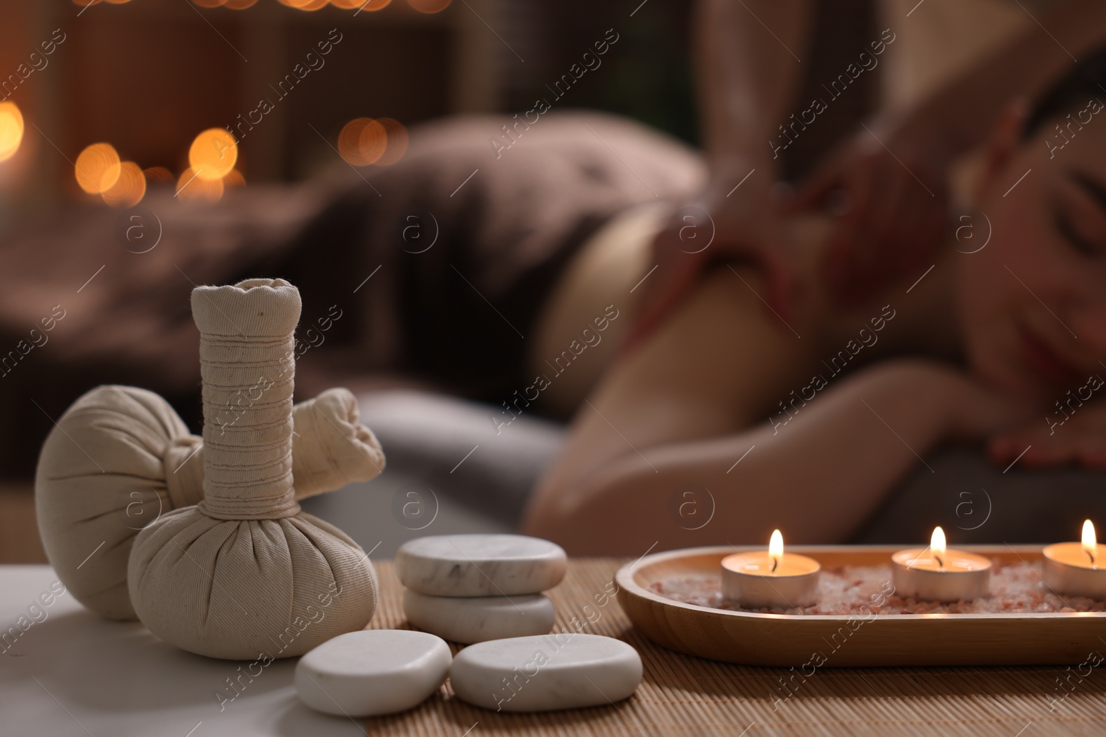 Photo of Spa therapy. Beautiful young woman lying on table during massage in salon, focus on burning candles, stones and herbal bags