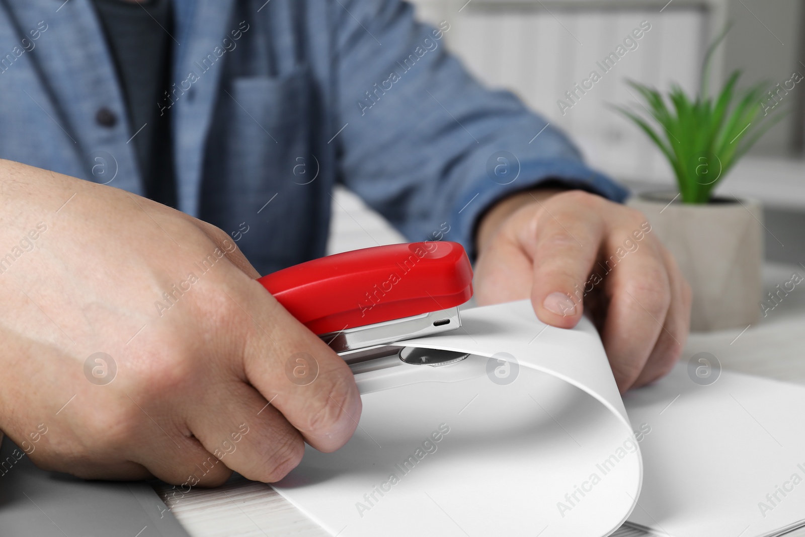 Photo of Man with papers using stapler at white table indoors, closeup