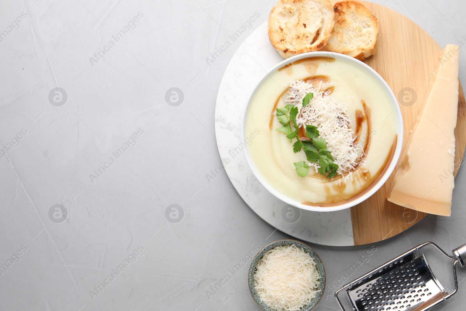 Photo of Delicious cream soup with parmesan cheese, soy sauce in bowl and croutons on light grey table, flat lay. Space for text