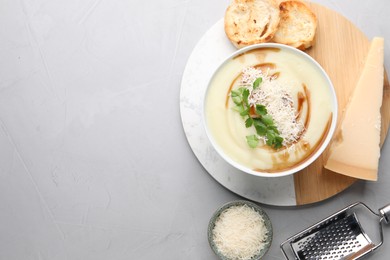 Delicious cream soup with parmesan cheese, soy sauce in bowl and croutons on light grey table, flat lay. Space for text