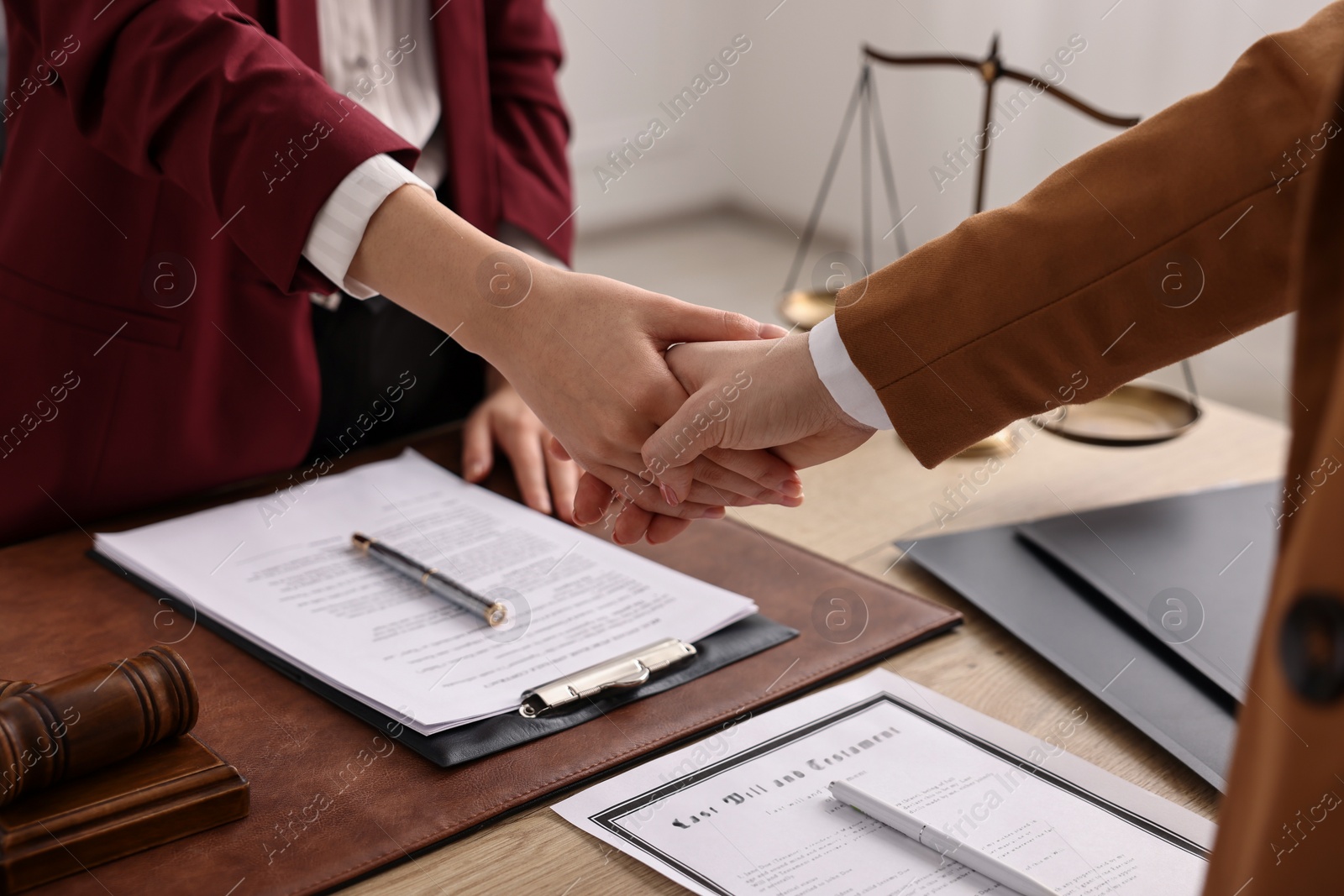 Photo of Notary shaking hands with client at wooden table in office, closeup