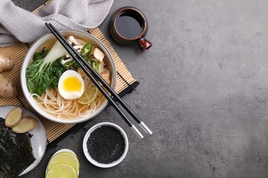 Vegetarian ramen, chopsticks and ingredients on grey table, flat lay. Space for text