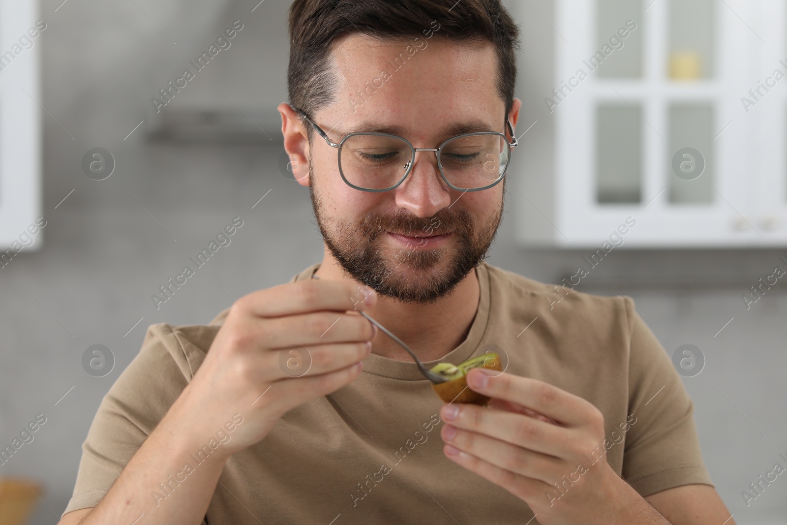 Photo of Man eating kiwi with spoon in kitchen