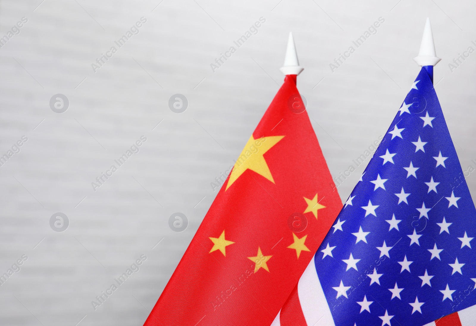 Photo of USA and China flags against white brick wall, closeup. International relations