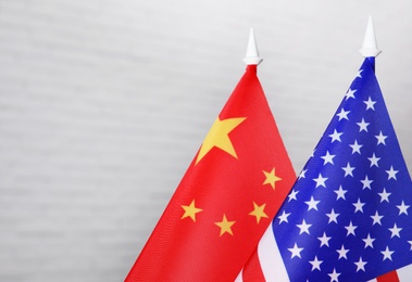 USA and China flags against white brick wall, closeup. International relations