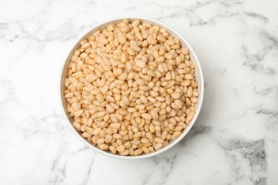 Photo of Bowl with pine nuts on marble background, top view