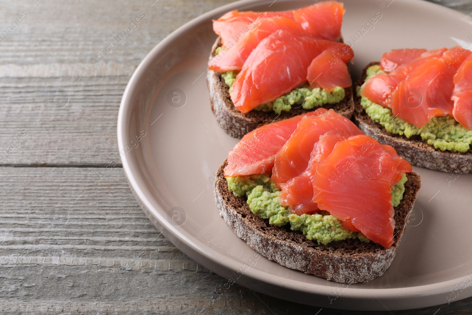 Photo of Delicious sandwiches with salmon and avocado on grey wooden table, closeup