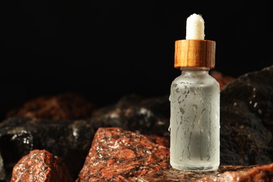 Photo of Bottle of face serum on wet stones against black background, closeup. Space for text