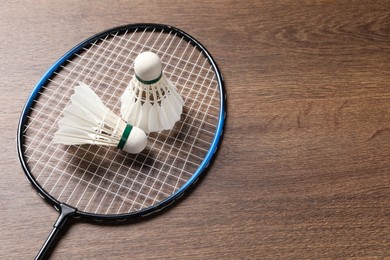 Photo of Feather badminton shuttlecocks and racket on wooden table, above view. Space for text