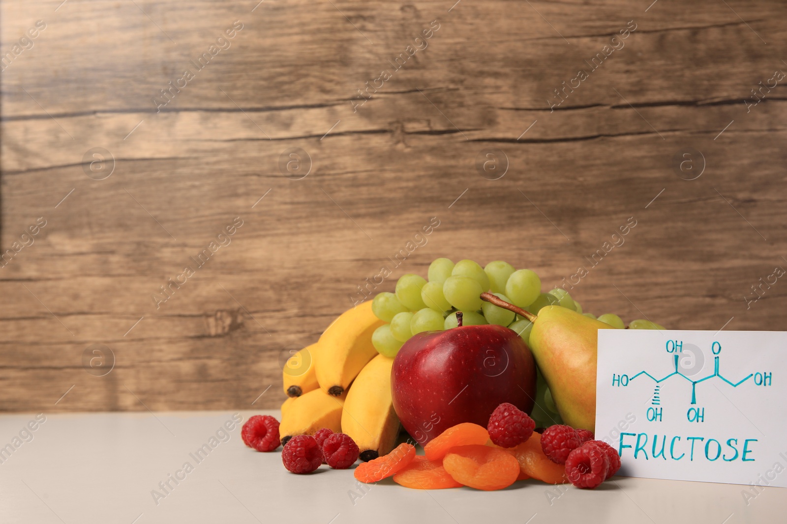 Photo of Card with word Fructose, delicious ripe fruits, raspberries and dried apricots on beige table, space for text