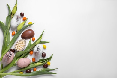 Photo of Flat lay composition with tulips, chocolate eggs and candies on white background, space for text. Easter celebration