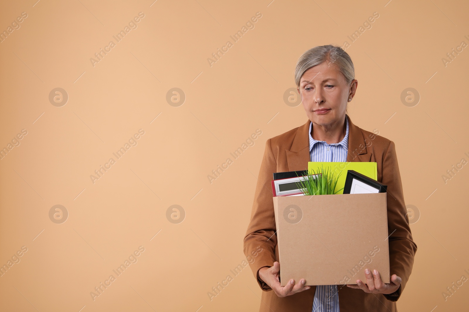 Photo of Unemployed senior woman with box of personal office belongings on beige background. Space for text