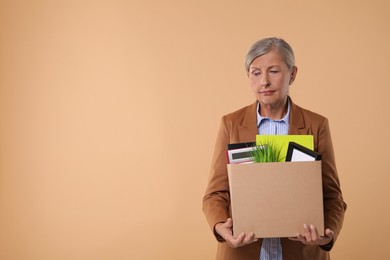 Photo of Unemployed senior woman with box of personal office belongings on beige background. Space for text