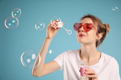 Young woman blowing soap bubbles on light blue background