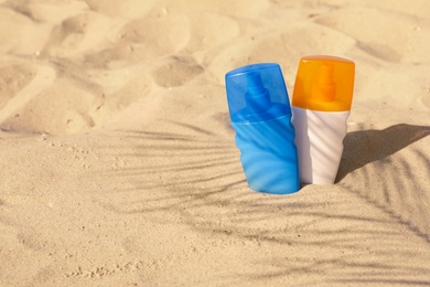 Bottles of sunblock in beach sand. Space for text