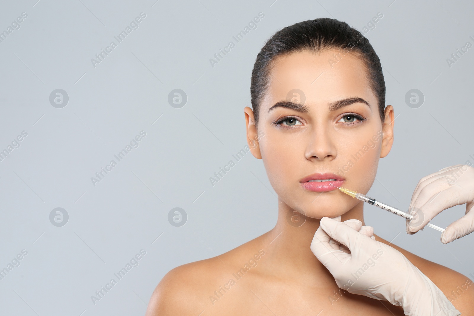 Photo of Young woman getting lips injection on grey background, space for text. Cosmetic surgery