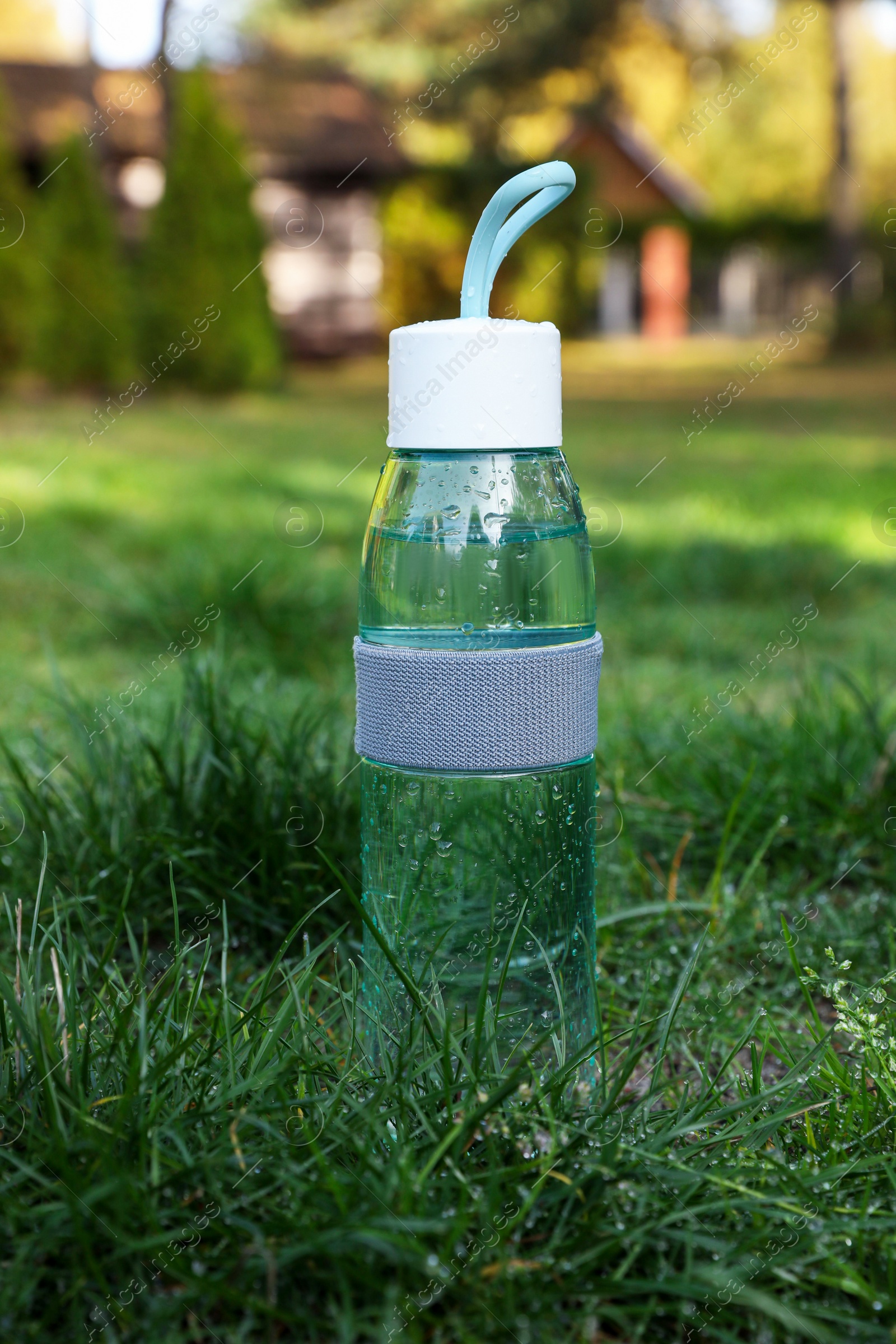 Photo of Glass bottle of fresh water on green grass outdoors