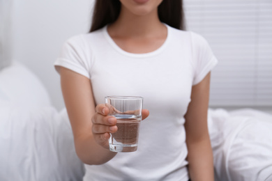 Woman holding glass of water in bedroom, closeup