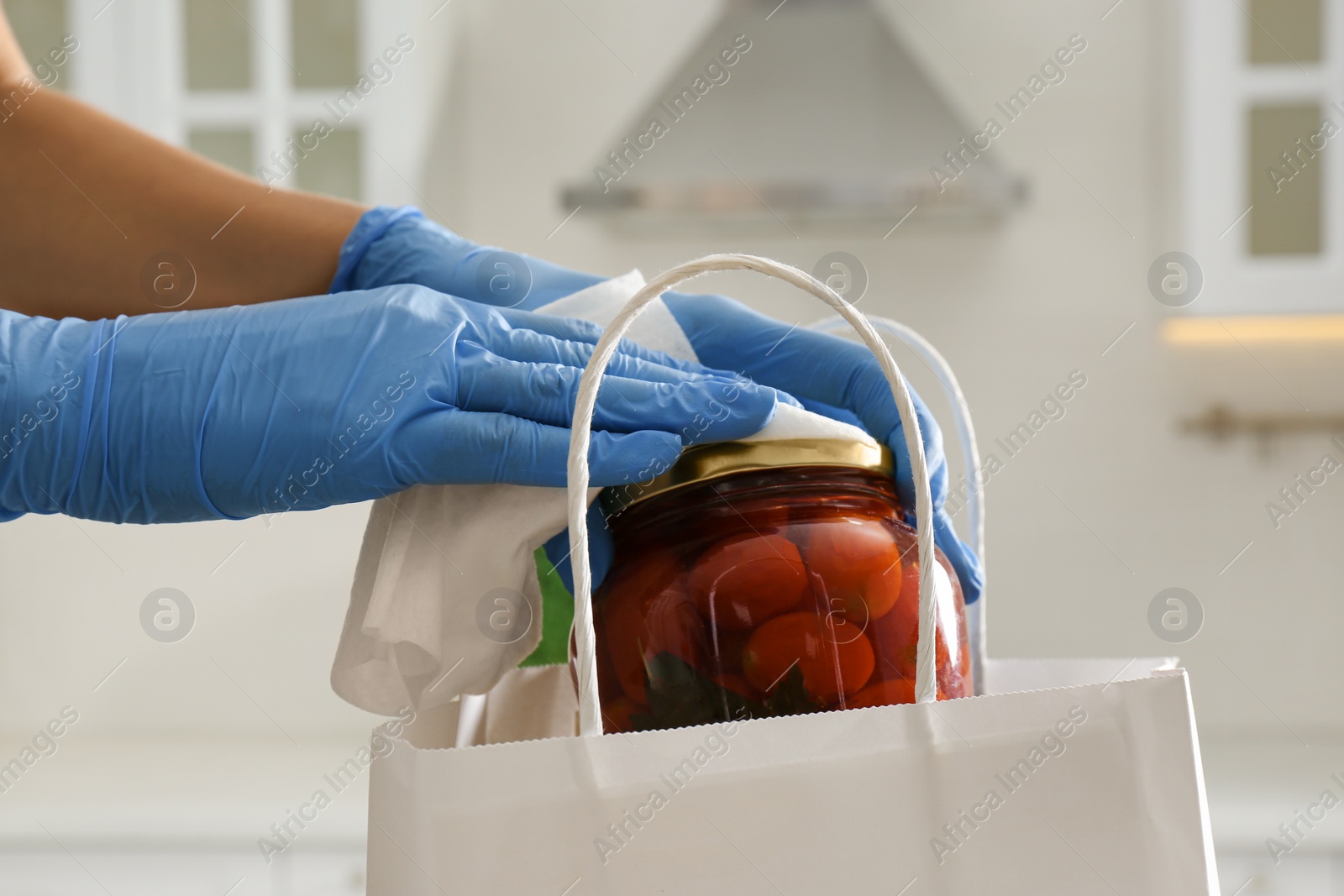 Photo of Woman cleaning newly purchased jar of pickled tomatoes with antiseptic wipe indoors, closeup. Preventive measures during COVID-19 pandemic