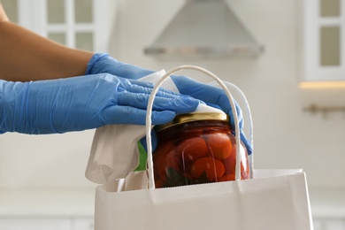 Photo of Woman cleaning newly purchased jar of pickled tomatoes with antiseptic wipe indoors, closeup. Preventive measures during COVID-19 pandemic