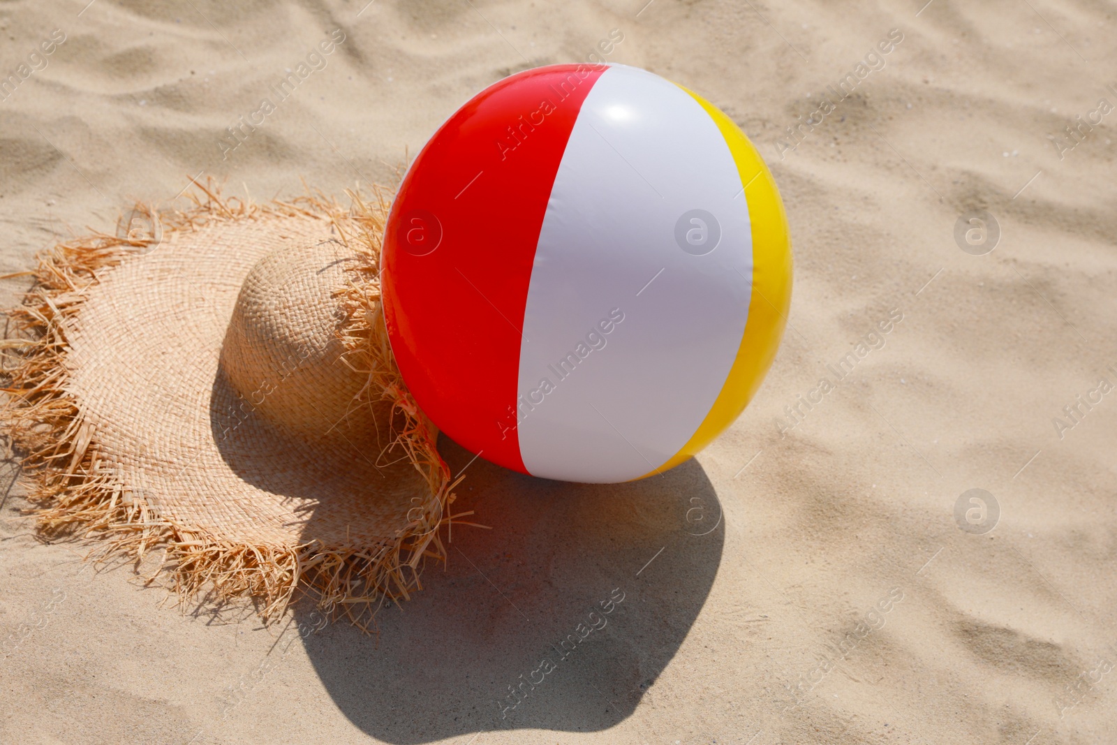 Photo of Straw hat and beach ball on sand outdoors