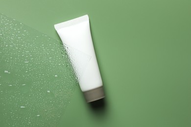 Tube with moisturizing cream on wet green surface, top view