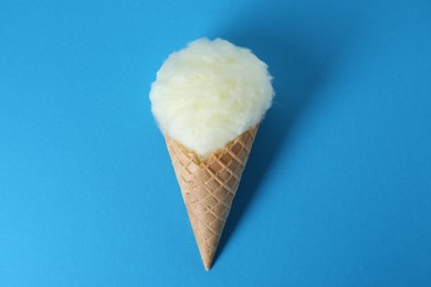 Sweet cotton candy in waffle cone on blue background, top view