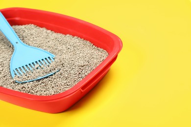 Photo of Cat litter tray with filler and scoop on yellow background, closeup. Space for text