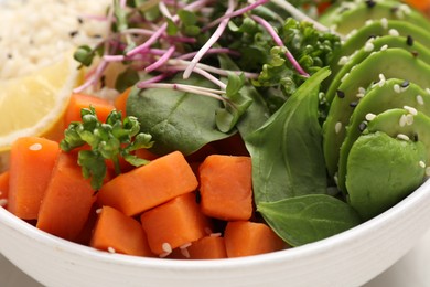 Delicious vegan bowl with avocados, carrots and microgreens on grey table, closeup