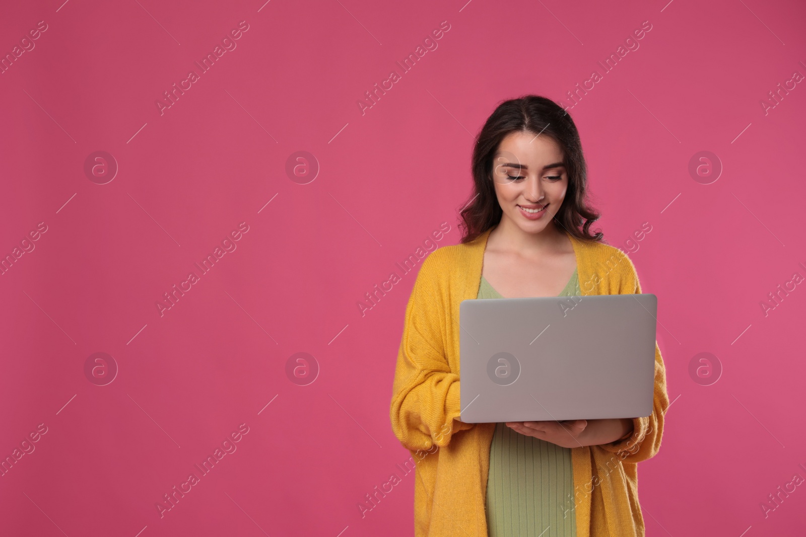 Photo of Young woman with laptop on pink background. Space for text