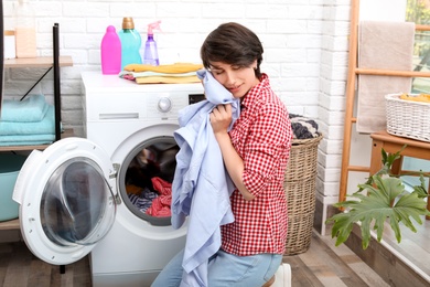 Young woman getting out clean clothes from washing machine at home