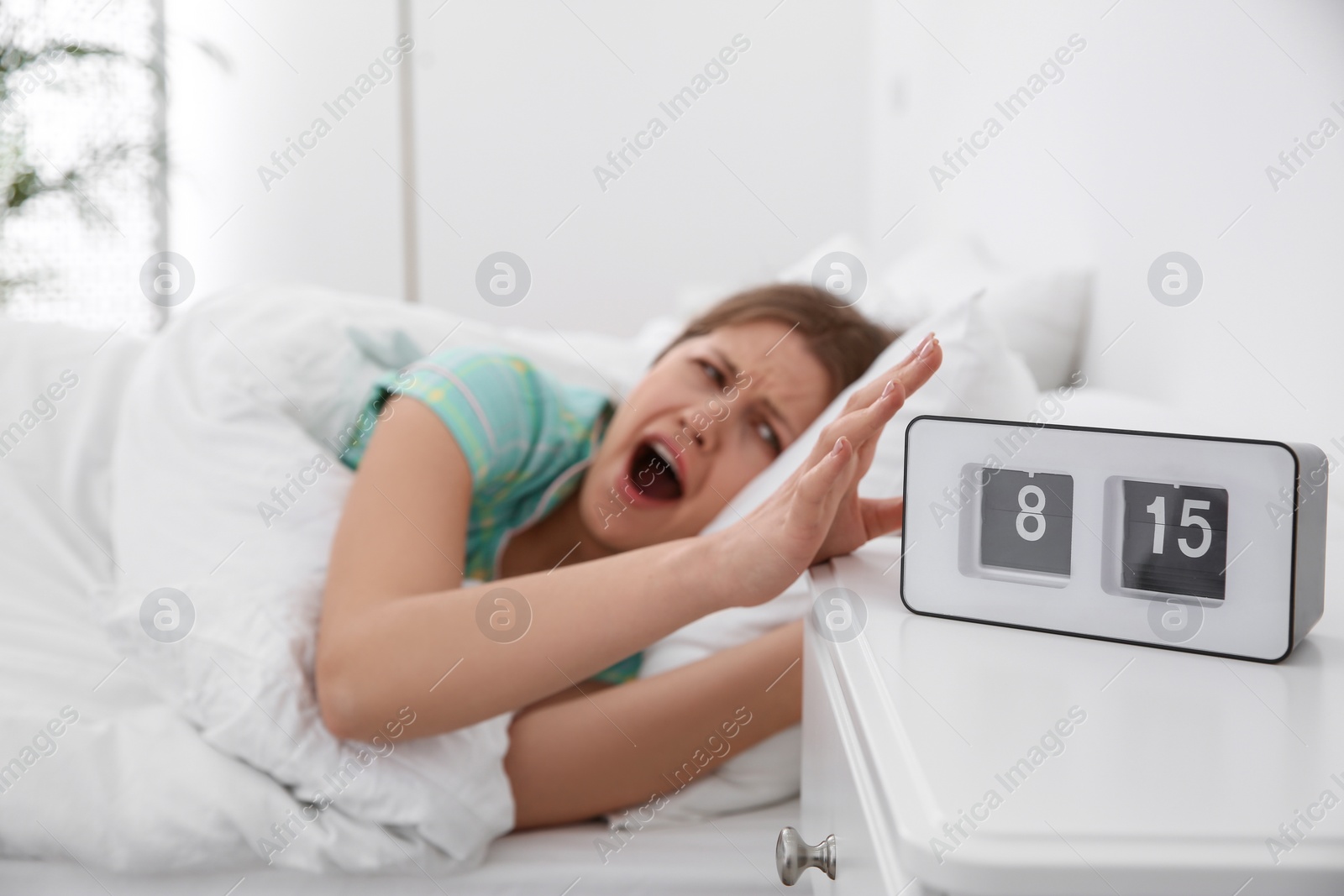 Photo of Clock and sleepy young woman at home in morning, focus on hand