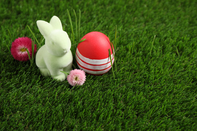 Colorful Easter egg, rabbit and daisy flowers on green grass. Space for text