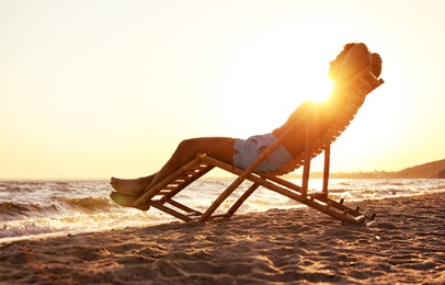 Young man relaxing in deck chair on beach near sea