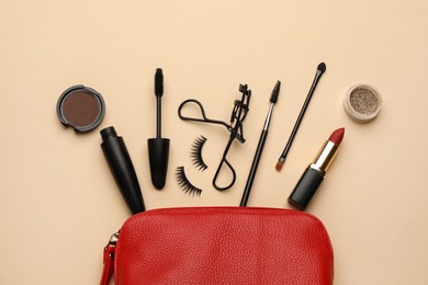 Cosmetic bag with eyelash curler and makeup products on beige background, flat lay