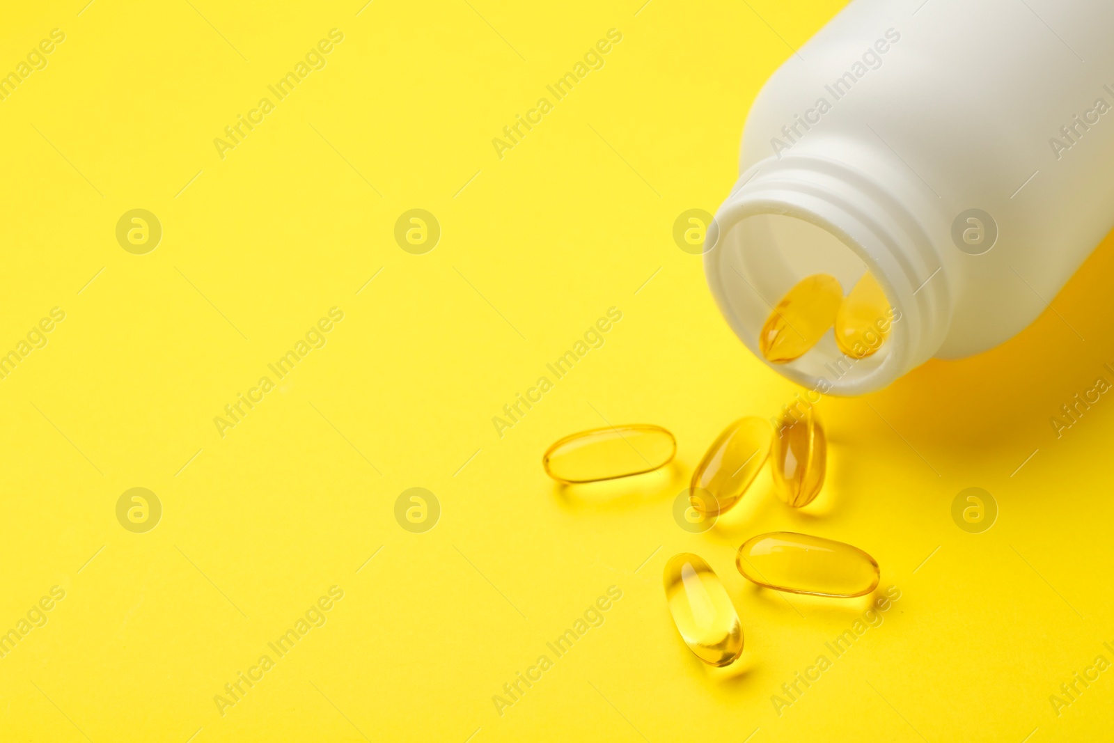 Photo of Softgel capsules and bottle on yellow background, closeup. Space for text